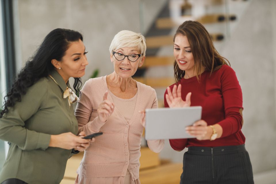 Three colleagues talking and sharing ideas over a tablet in a bright office