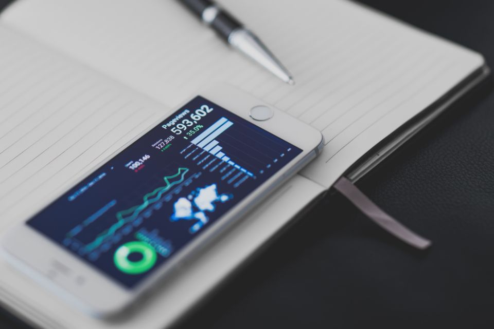 Smartphone on a desk displaying a data dashboard beside a notebook and pen
