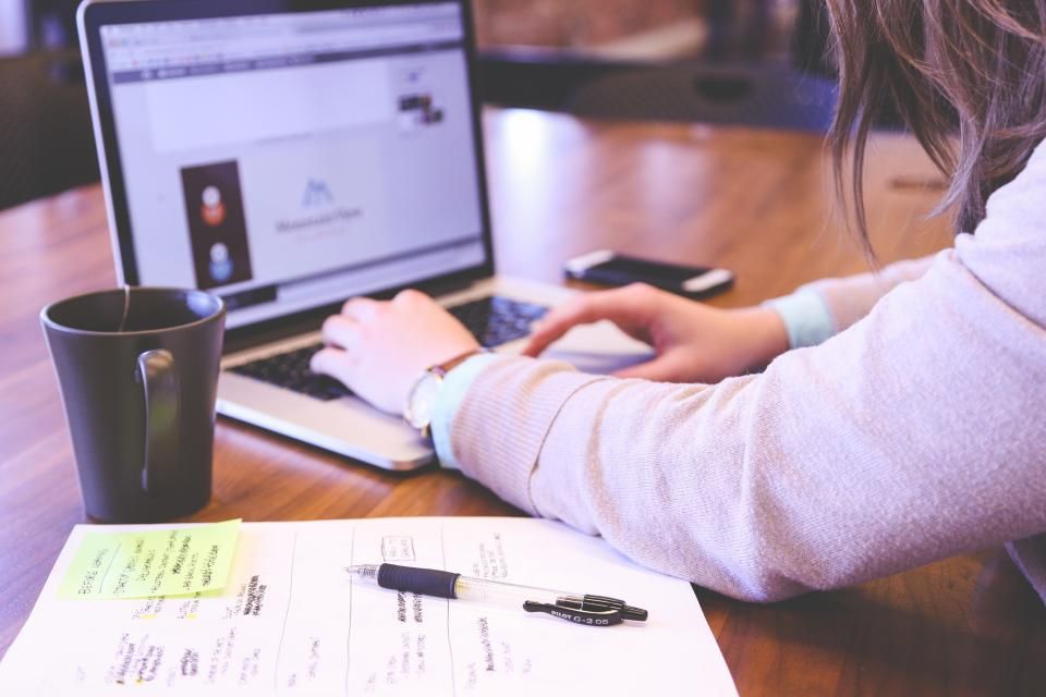 Person typing on a laptop next to printed notes and a coffee mug