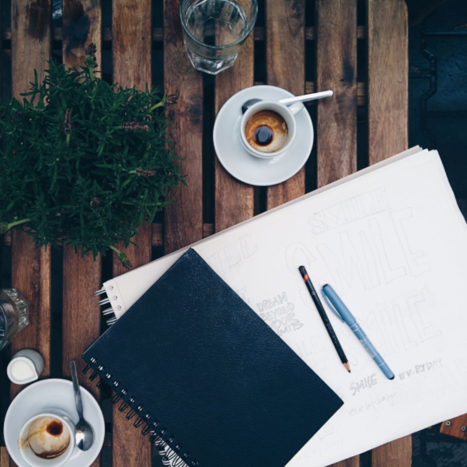 A notebook, sketches and a cup of coffee on a wooden table