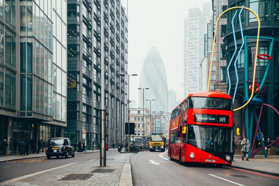 A red London double-decker bus driving along a city street lined with modern buildings