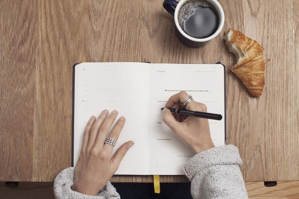 Person writing notes in a notebook beside a cup of coffee